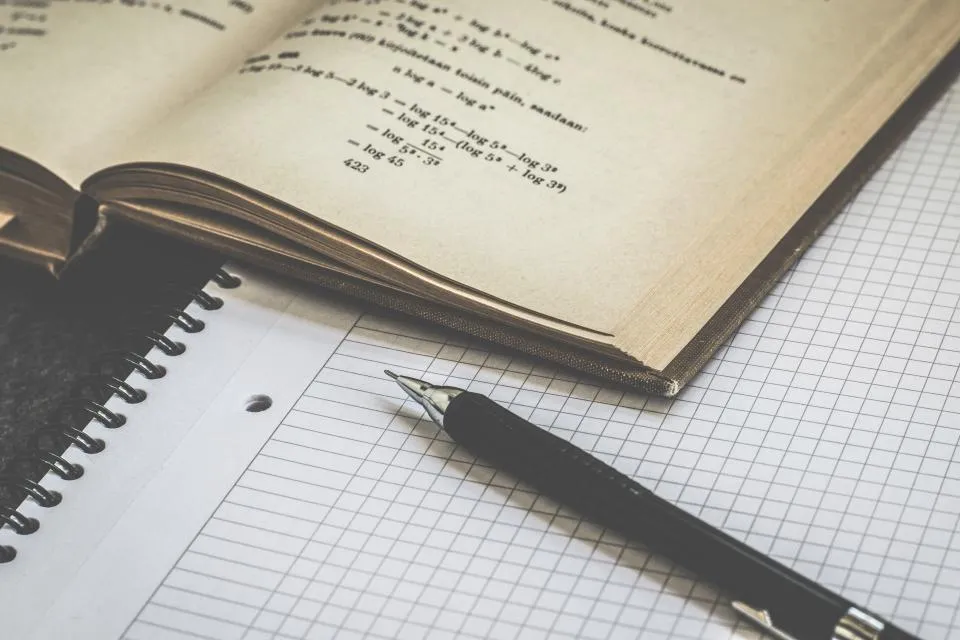 A notebook of handwritten equations beside squared graph paper and a pen